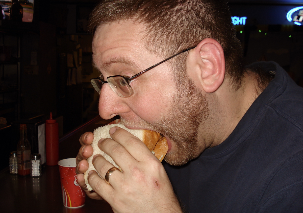 A dude takes a very big bite of a much bigger sandwich