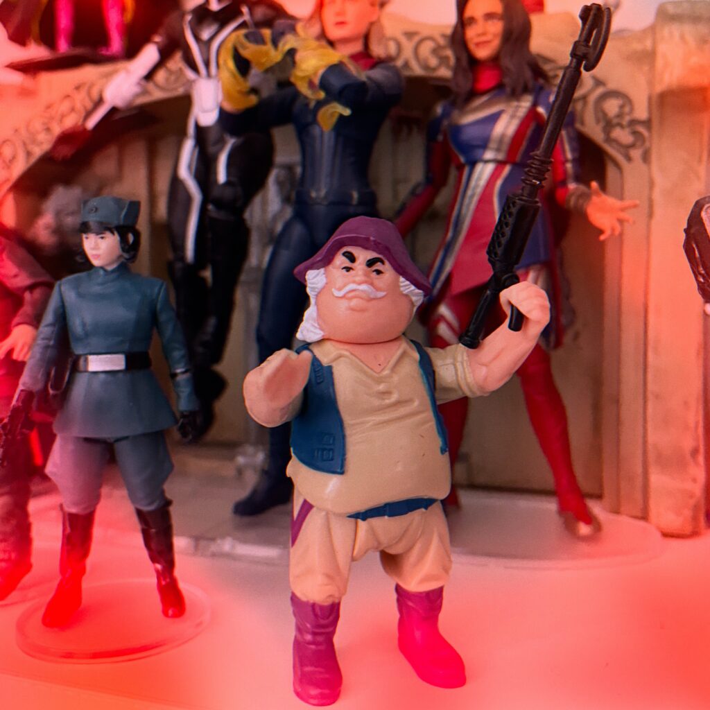 A retro action figure of a grizzled prospector with a white mustache, purple hat, and (for some reason) a big gun.