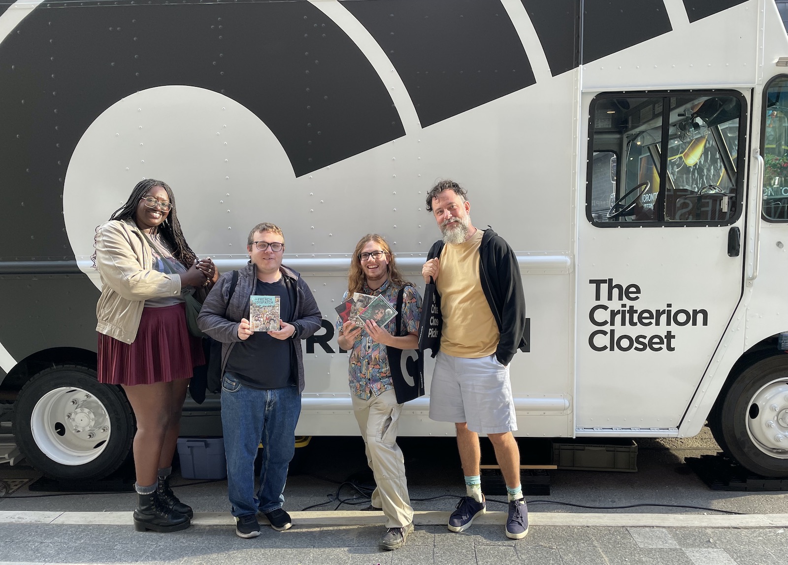 Four weirdos standing in front of the mobile Criterion Closet, a camper van.