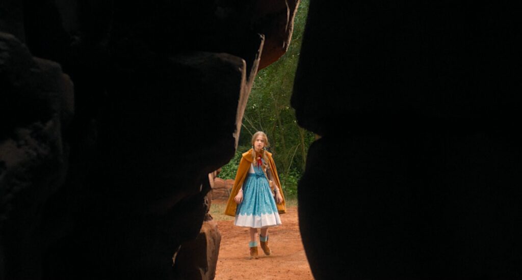 Holly Wheeler, still blonde, still 10 (?), now wears a bright blue dress with an ochre cloak and big rainbowy boots.