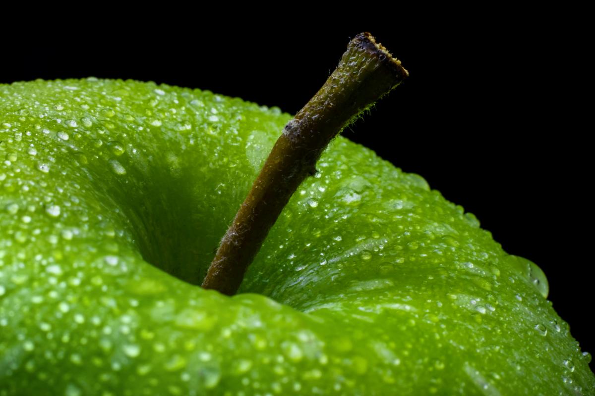 The top of a bright green apple, dripping with condensation.
